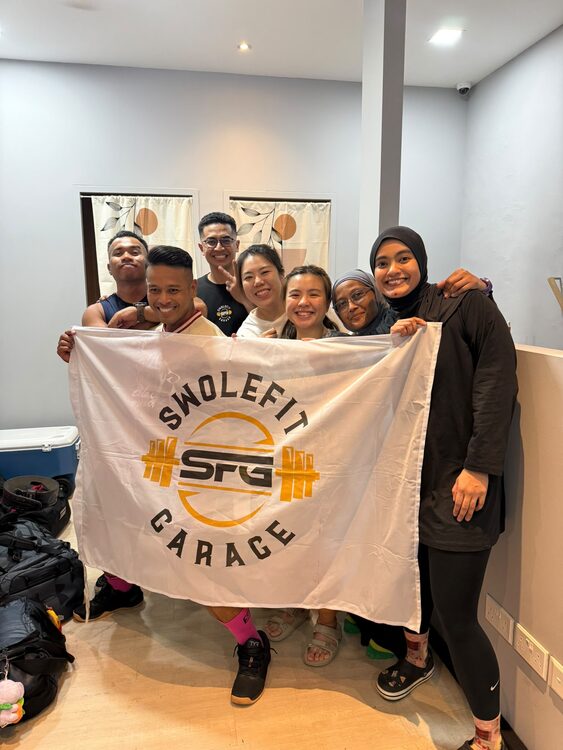 A group of SwoleFit Garage members holding an SFG flag together