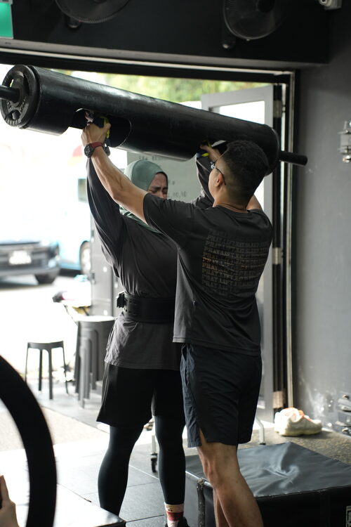 A coach assisting a member on a log bar exercise at SwoleFit Garage